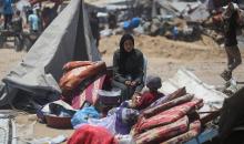 امرأة وطفل يجلسان على متعلقات تم إنقاذها بينما يتفقد فلسطينيون خياماً مدمرة في خان يونس (أ.ف.ب).jpeg