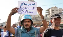 صحفي فلسطيني يحمل لافتة تعبر عن أوضاع غزة المأساوية.webp