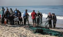 صيادون فلسطينيون نازحون يجمعون صيدهم من الشباك التي جلبوها إلى الشاطئ في دير البلح، في وسط قطا (4).jpg