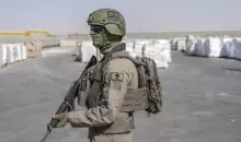 جندي إسرائيلي بجانب طرود مساعدات إنسانية تنتظر استلامها بمعبر كرم أبو سالم في قطاع غزة.webp