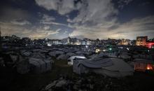 يسير فلسطينيون في أحد شوارع مدينة غزة، بينما يكافح النازحون في خيامهم لمواجهة الظلام، يتدفؤون ويطهون طعامهم بالحطب، محرومين حتى من أبسط مقومات الحياة، 19 يناير/كانون الثاني 2026. صورة: عمر أشتوي