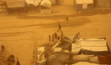 فلسطينيون يسيرون وسط عاصفة رملية في مخيم خيام يؤوي فلسطينيين نزحوا خلال العدوان الإسرائيلي الذي استمر عامين، في خان يونس جنوب قطاع غزة، 14 مارس/آذار 2026. تصوير: طارق محم