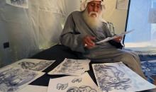 محمد زملط، رجل فلسطيني مسنّ اقتلعته الحرب من مخيم جباليا في شمال قطاع غزة، يحمل اليوم ريشته كوسيلة للبقاء، لا للفن فقط. في خيمته المتواضعة بمخيم البريج وسط القطاع، 12 أبريل/نيسان 2026، عدسة: يوسف أبو وطفة