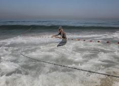 صيادون فلسطينيون نازحون يجمعون صيدهم من الشباك التي جلبوها إلى الشاطئ في دير البلح، في وسط قطا.jpg