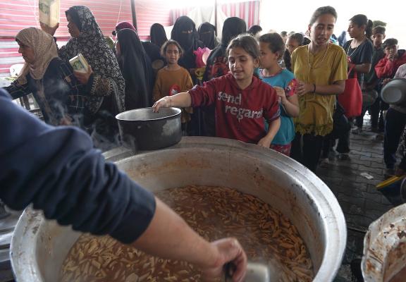 فلسطينيون نازحون، بينهم نساء وأطفال، يتجمعون لتلقي وجبات طعام من مطبخ خيري في مخيم النصيرات للاجئين وسط قطاع غزة، في 21 مايو/أيار 2026. الصورة: رمزي أبو عامر.