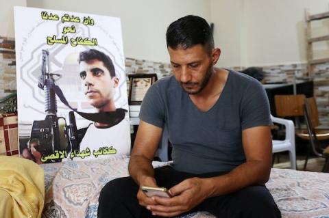     يحيى الزبيدي، شقيق الأسير زكريا الزبيدي يجلس بجانب صورة أخيه في منزلهم في مدينة جنين بالضفة الغربية