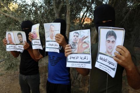 ملثمون فلسطينيون يجهزون بالونات تحمل صور الأسرى الستة قبل إطلاقها باتجاه إسرائيل في خانيونس
