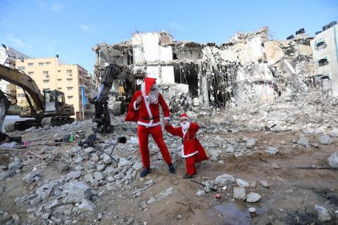   فلسطيني وابنه يرتديان زي بابا نويل يسيران بالقرب من ركام برج الجوهرة الذي تعرض للقصف خلال التصعيد الإسرائيلي الأخير على قطاع غزة.