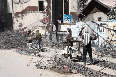 عمال فلسطينيون يقومون بتصويب قضبان الحديد كجزء من إعادة تدوير مواد البناء التي تم إنقاذها من المباني التي دمرت خلال التصعيد الأخير على قطاع غزة، في مدينة غزة
