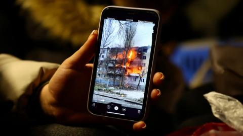 امرأة تنظر إلى صورة لحريق شقة صديقتها على هاتفها، أثناء انتظارها ركوب القطار إلى كراكوف بعد عبور الحدود من أوكرانيا إلى بولندا. 09/03/2022. (فابريزيو بينش/ رويترز)