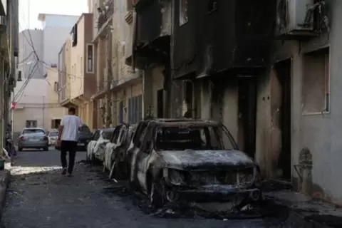 رجل يسير إلى جانب سيارات متفحمة بعد يوم من اشتباكات شهدتها طرابلس في ليبيا يوم السبت. تصوير: حازم أحمد - رويترز