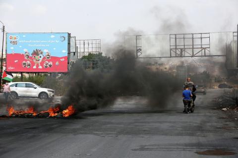 متظاهرون يحملون الأعلام الفلسطينية ويحرقون الإطارات على حاجز حوارة احتجاجا على استمرار الحصار الإسرائيلي على مدينة نابلس