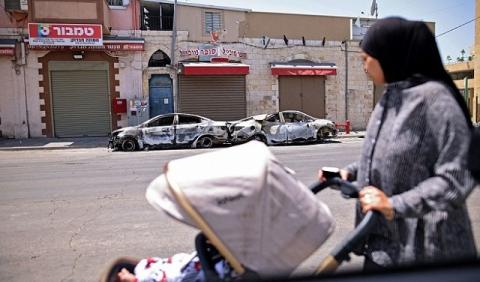 امرأة تنظر إلى سيارات محترقة في اللد، بهبة الكرامة (Getty Images)