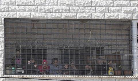 عائلات فلسطينية من بلدة حوارة تنظر بخشية من وراء ستار حديدي يحمي من هجمات المستوطنين .. تصوير - أيمن نوباني.jpg