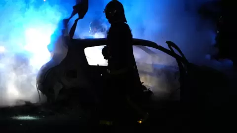 رجل إطفاء يسير قرب سيارة متفحمة بعدما أحرقها متظاهرون في ضاحية نانتير في غرب باريس في 27 حزيران/يونيو 2023 بعد قتل شرطي لمراهق عند نقطة تفتيش مرورية - زكريا عبد الكافي / ا ف ب