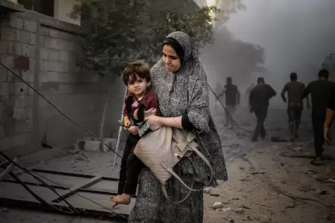 فلسطينية تحمل طفلها وسط بنايات دمرها الاحتلال الإسرائيلي في مخيم المغازي بغزة (وكالة الأناضول).webp