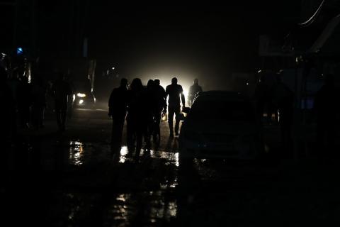 أشخاص يسيرون في شارع مظلم لجأت إليه عائلات فلسطينية نازحة بسبب الهجمات الإسرائيلية المستمرة على دير البلح بغزة في 23 مارس 2024