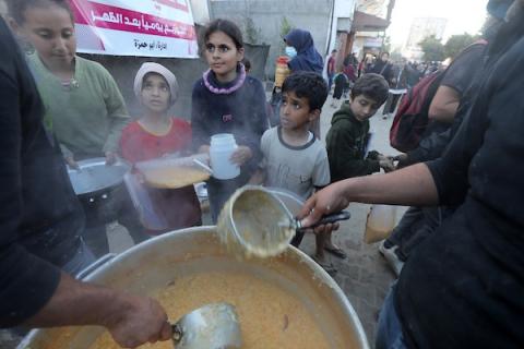 نازحون فلسطينيون يتجمعون لتلقي الطعام الذي تبرعت به مؤسسة خيرية قبل وجبة الإفطار، في اليوم الثالث من شهر رمضان المبارك، في دير البلح في وسط قطاع غزة في 13 مارس 2024 - بواسطة: عمر اشتيوي