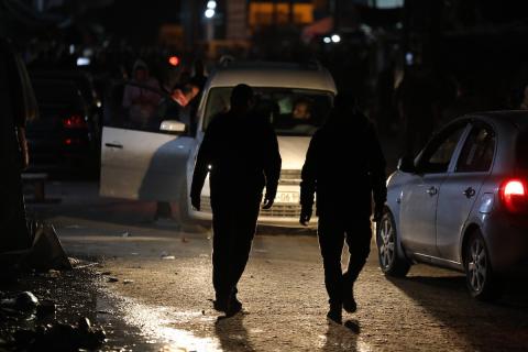 أشخاص يسيرون في شارع مظلم لجأت إليه عائلات فلسطينية نازحة بسبب الهجمات الإسرائيلية المستمرة على دير البلح بغزة في 23 مارس 2024