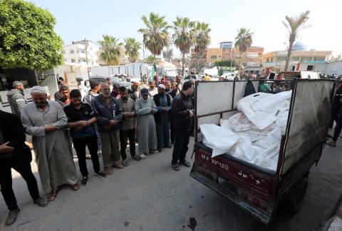 فلسطينيون يصلون بالقرب من جثامين المجهولين الذين استشهدوا بقصف إسرائيلي على غزة في دير البلح وسط قطاع غزة قبل دفنهم