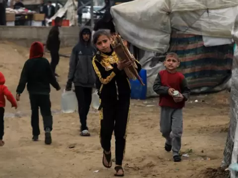 فتاة فلسطينية تحمل حزمة من الحطب في مخيم مؤقت بمدينة رفح.webp