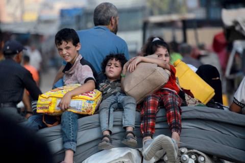 أطفال فلسطينيون يركبون على ظهر عربة وهم يحملون أمتعتهم في غزة (أ.ف.ب).jpeg