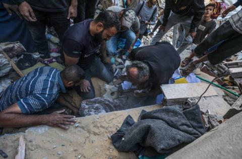 فلسطينيون ينتشلون جثامين الضحايا من تحت أنقاض منزل عائلة شناعة المدمر في أعقاب غارة جوية إسرائيلية على مخيم المغازي للاجئين في قطاع غزة (إ.ب.أ)