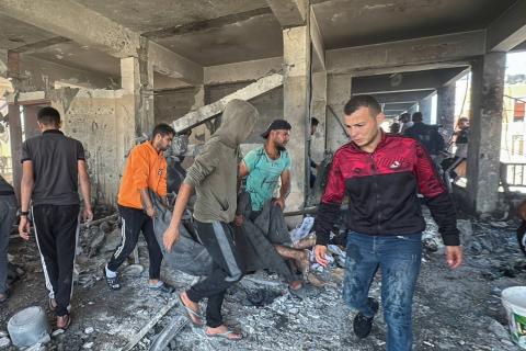 أشخاص يحملون جثة فلسطيني قُتل في غارة إسرائيلية على مدرسة تؤوي النازحين وسط قطاع غزة (رويترز).jpeg