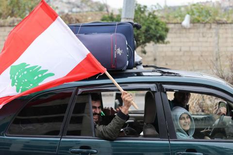 رجل يلوِّح بعَلم لبنان في مدينة صيدا بالجنوب بينما يتجه النازحون إلى منازلهم بعد سريان وقف إطلاق النار (أ.ف.ب).jpeg