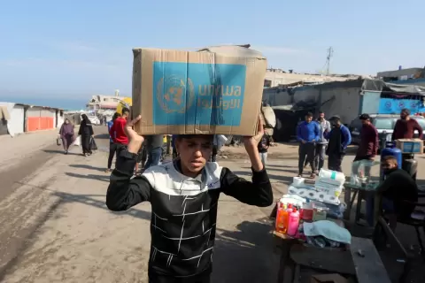 فلسطيني يحمل صندوق مساعدات وزّعته وكالة «الأونروا» في دير البلح بقطاع غزة (رويترز).webp