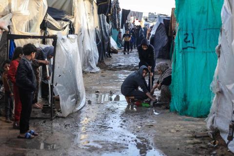 نازحون فلسطينيون يتجمعون وسط خيام غمرتها الأمطار الغزيرة في رفح (أ.ف.ب)