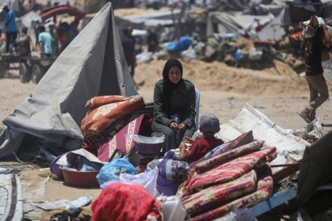 امرأة وطفل يجلسان على متعلقات تم إنقاذها بينما يتفقد فلسطينيون خياماً مدمرة في خان يونس (أ.ف.ب).jpeg