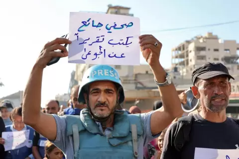 صحفي فلسطيني يحمل لافتة تعبر عن أوضاع غزة المأساوية.webp