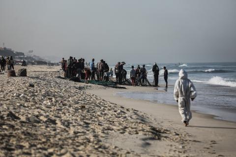 صيادون فلسطينيون نازحون يجمعون صيدهم من الشباك التي جلبوها إلى الشاطئ في دير البلح، في وسط قطا (3).jpg