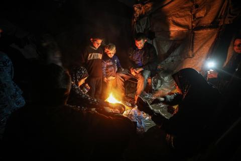 يسير فلسطينيون في أحد شوارع مدينة غزة، بينما يكافح النازحون في خيامهم لمواجهة الظلام، يتدفؤون ويطهون طعامهم بالحطب، محرومين حتى من أبسط مقومات الحياة، 19 يناير/كانون الثاني 2026. صورة: عمر أشتوي