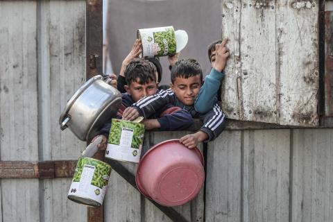 أطفال فلسطينيون ينتظرون وجبة ساخنة، توزعها إحدى المنظمات الخيرية، في ظل استمرار أزمة الغذاء بسبب محدودية المساعدات الإنسانية في مخيم النصيرات للاجئين وسط قطاع غزة، في 10 يناير/كانون الثاني 2026. صورة: معز صالحي