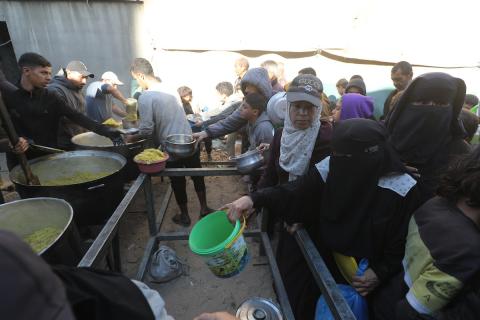 يتجمع فلسطينيون لتناول وجبة ساخنة وزعتها إحدى الجمعيات الخيرية، وسط أزمة غذائية مستمرة بسبب محدودية المساعدات الإنسانية خلال شهر رمضان في مخيم النصيرات للاجئين وسط قطاع غزة. ٢٣ فبرايرشباط ٢٠٢٦. تصوير معز صالحي