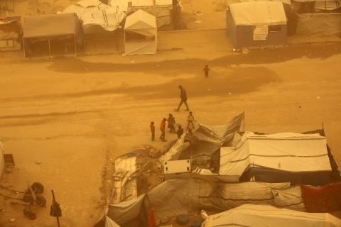 فلسطينيون يسيرون وسط عاصفة رملية في مخيم خيام يؤوي فلسطينيين نزحوا خلال العدوان الإسرائيلي الذي استمر عامين، في خان يونس جنوب قطاع غزة، 14 مارس/آذار 2026. تصوير: طارق محم