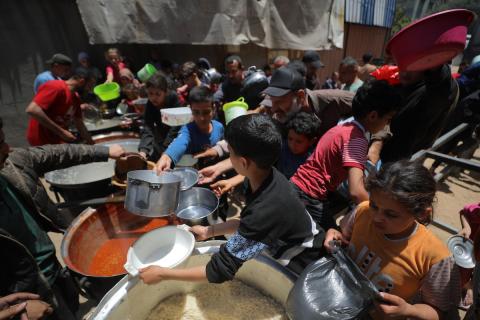 فلسطينيون نازحون، بينهم نساء وأطفال، يتجمعون لتلقي وجبات طعام من مطبخ خيري في مخيم النصيرات للاجئين وسط قطاع غزة، في 13 مايو/أيار 2026، وسط تراجع الإمدادات الإنسانية واستمرار الإغلاق الجزئي للمعابر الحدودية. تصوير: حسن الجديدي