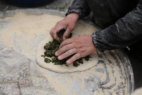 امرأة فلسطينية تُعدّ الخبز على نار الحطب في شارع رئيسي بنابلس شمال الضفة الغربية، 2 مايو/أيار 2026، خلال معرض ملح الأرض  للتراث الفلسطيني (تصوير: محمد ناصر)