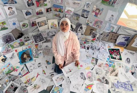 الفنانة الفلسطينية رنيم ناصر تعرض رسوماتها داخل خيمتها في دير البلح وسط قطاع غزة، موثّقةً بالألوان معاناة الحرب والنزوح. تصوير: يوسف أبو وطفة