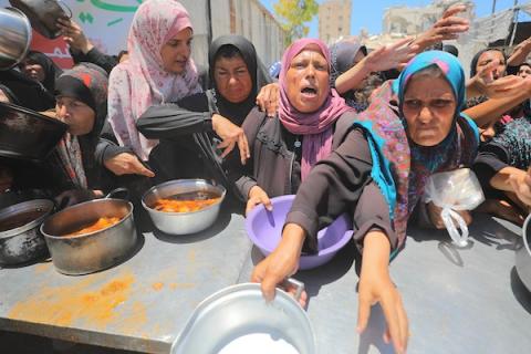 نساء وأطفال فلسطينيون نازحون ينتظرون الحصول على وجبات طعام وزعتها منظمات خيرية في مدينة غزة، وسط تفاقم الأزمة الإنسانية وارتفاع درجات الحرارة، في 22 يونيو/حزيران 2026. تصوير: حسن الجدي