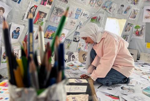 الفنانة الفلسطينية رنيم ناصر تعرض رسوماتها داخل خيمتها في دير البلح وسط قطاع غزة، موثّقةً بالألوان معاناة الحرب والنزوح. تصوير: يوسف أبو وطفة