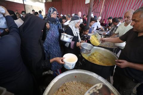 فلسطينيون نازحون، بينهم نساء وأطفال، يتجمعون للحصول على وجبات ساخنة وزّعها مطبخ خيري في مخيم النصيرات للاجئين وسط قطاع غزة، في 13 يونيو/حزيران 2026، وسط نقص حاد في الإمدادات الغذائية. تصوير: حسن الجديدي