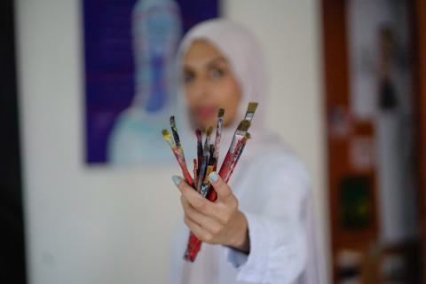 الفنانة نورة القصاص ترسم داخل غرفة بسيطة حولتها إلى مرسم في منزل أحد أقاربها بحي الشيخ رضوان في مدينة غزة، في 12 أغسطس/آب 2026. (تصوير: محمد أبو القمصان)