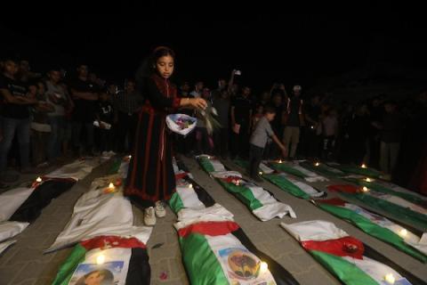 فلسطينيون يتجمعون حول رفات 106 ضحايا غُطيت بالأعلام الفلسطينية وأضيئت إلى جانبها الشموع، خلال مراسم وداع في حي الزيتون بمدينة غزة، 5 أيلول/سبتمبر 2026. تصوير: بلال أسامة