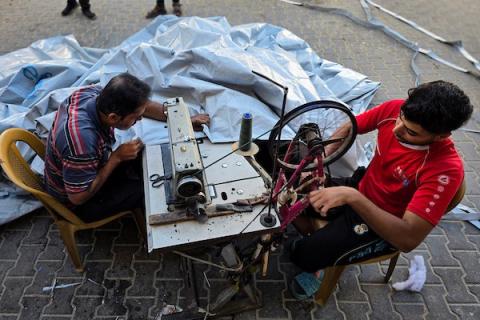 الخياط الفلسطيني شعبان الطباش يصلح أغطية بلاستيكية وقماشًا مشمعًا لتقوية خيام النازحين وحمايتها من برد الشتاء وأمطاره، في خان يونس جنوب قطاع غزة، 4 أكتوبر/تشرين الأول 2026. (تصوير: طارق محمد)