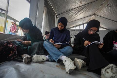 طلاب يتلقون دروسهم جلوسًا على الأرض داخل خيام تفتقر إلى المقاعد والتجهيزات المدرسية في مركز سرايا التعليمي بقطاع غزة، 11 أكتوبر/تشرين الأول 2026. (تصوير: محمد صالحة)
