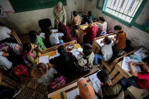 أطفال فلسطينيون يواصلون تعليمهم على مقاعد مصنوعة من صناديق المساعدات المُعاد تدويرها في مدينة غزة، وسط دمار المدارس ونقص المستلزمات التعليمية. (تصوير: محمد صالحة)