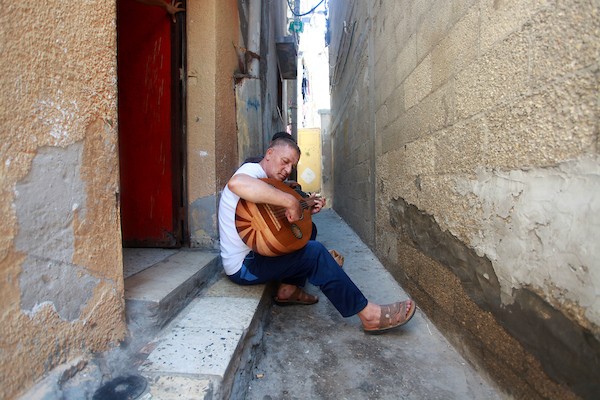 اللاجئ الفلسطيني كمال أبو غبن يعزف على آلة العود أثناء راحته في العمل